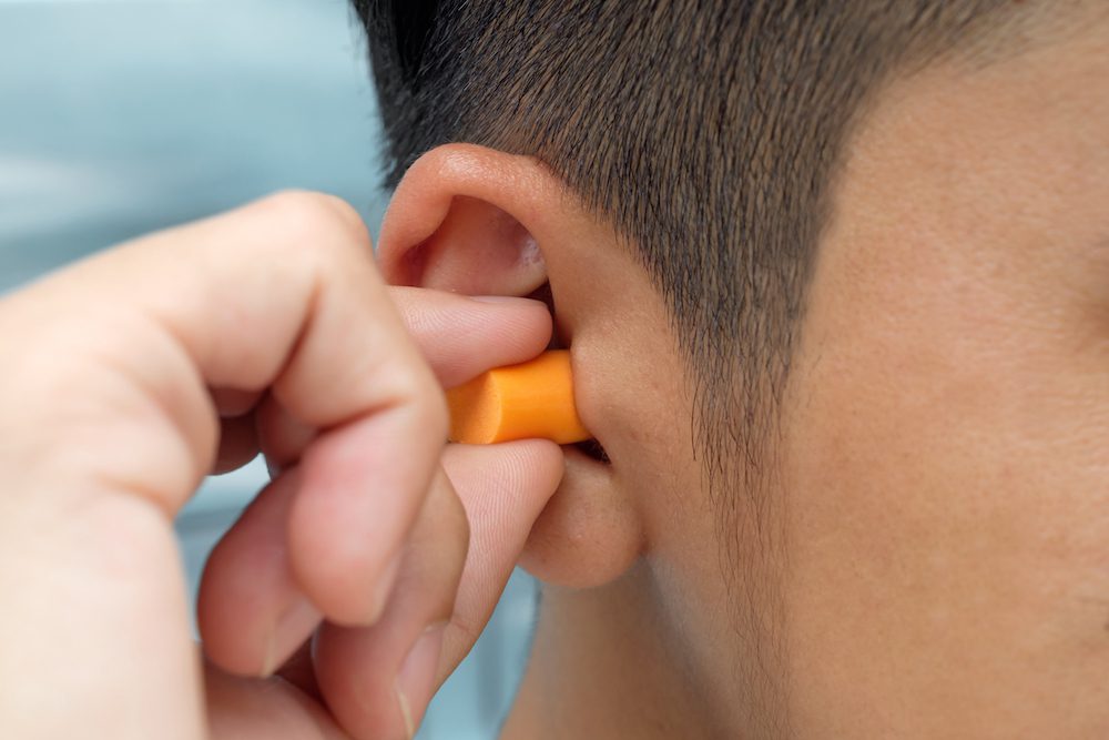 closeup of man inserting orange earplug into his right ear canal