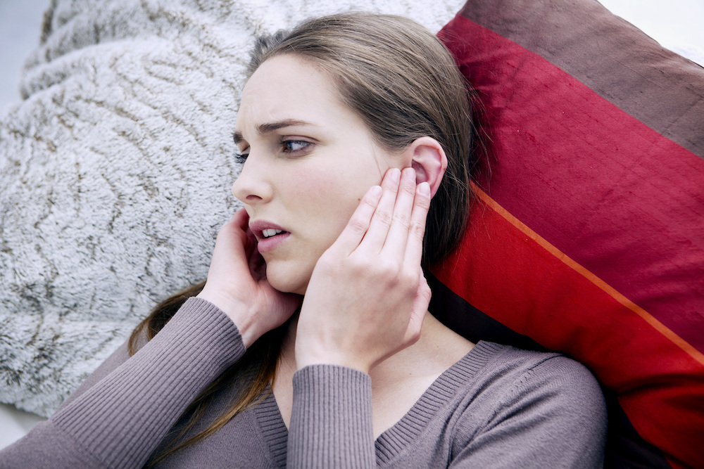 woman lying down in bed wearing sweater with head pains