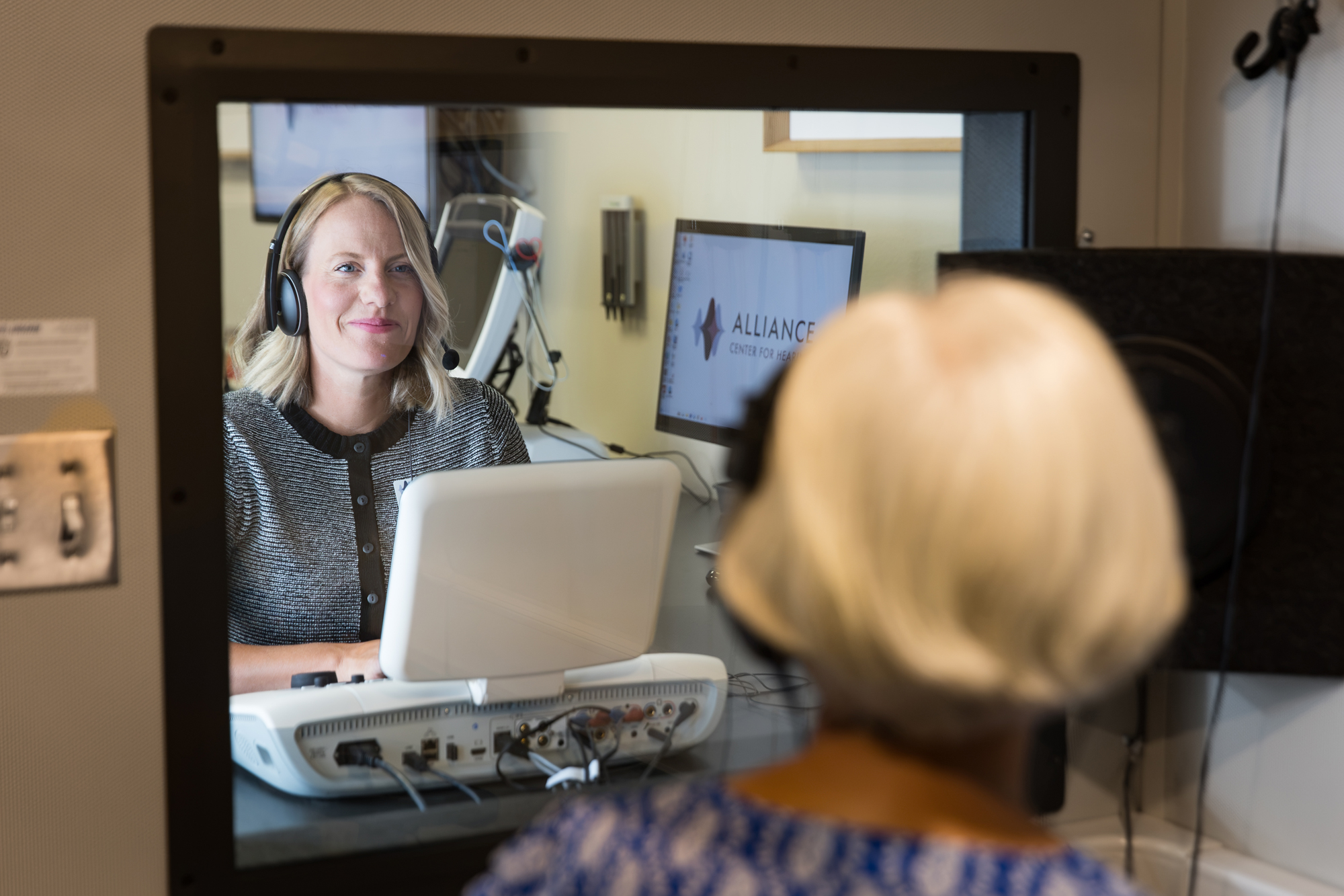 jessica leading a senior woman through hearing test in sound booth