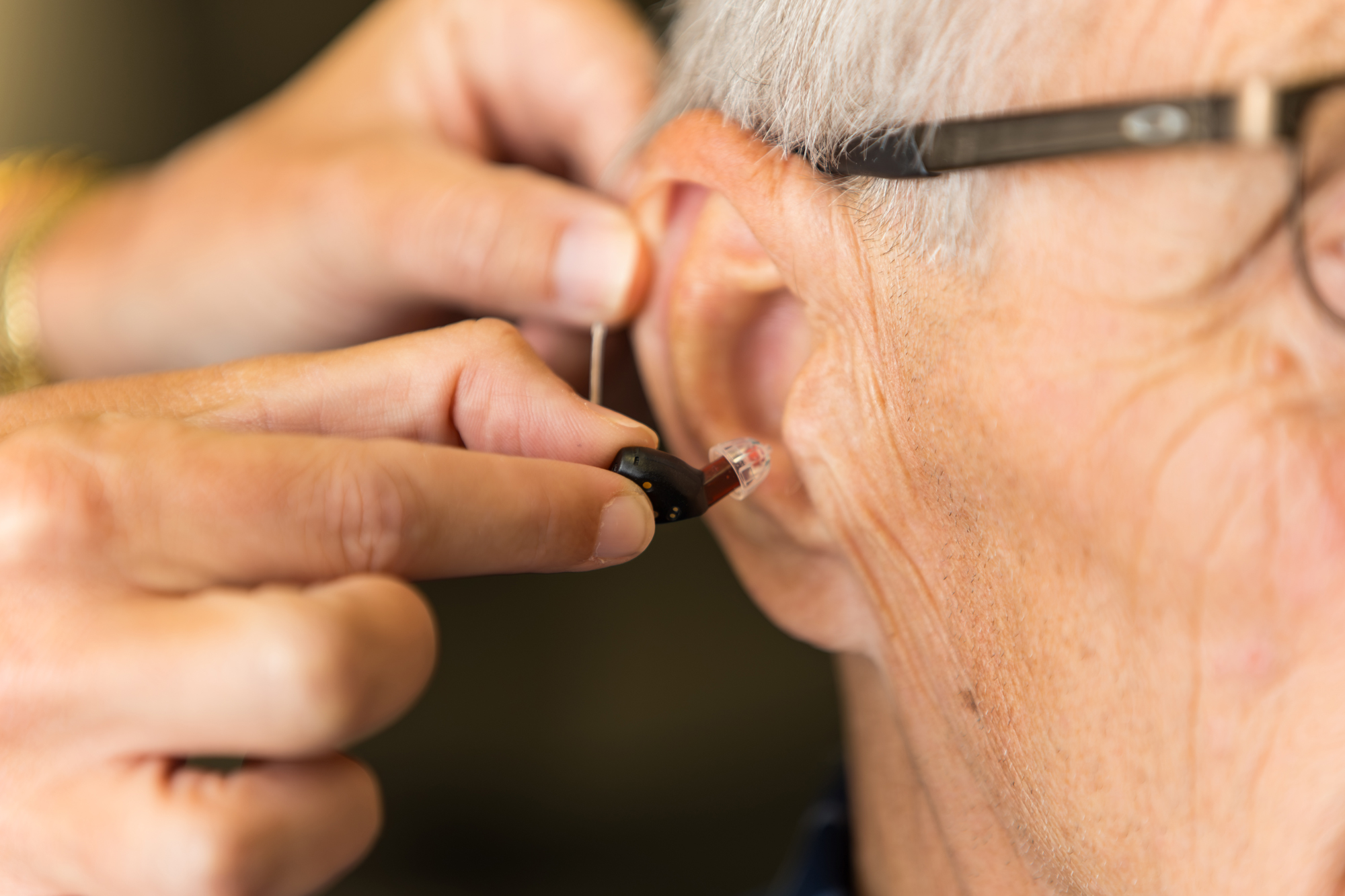 hearing care provider inserting hearing aid in mans ear canal