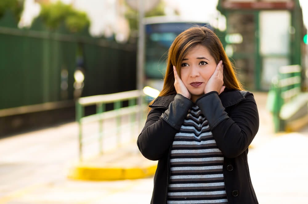 woman covering her ears with both hands on the street