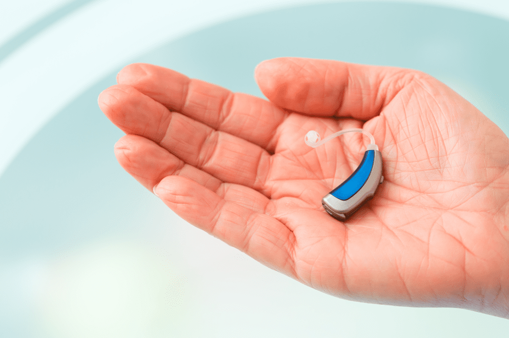a hearing aid held in a hand against a blue background