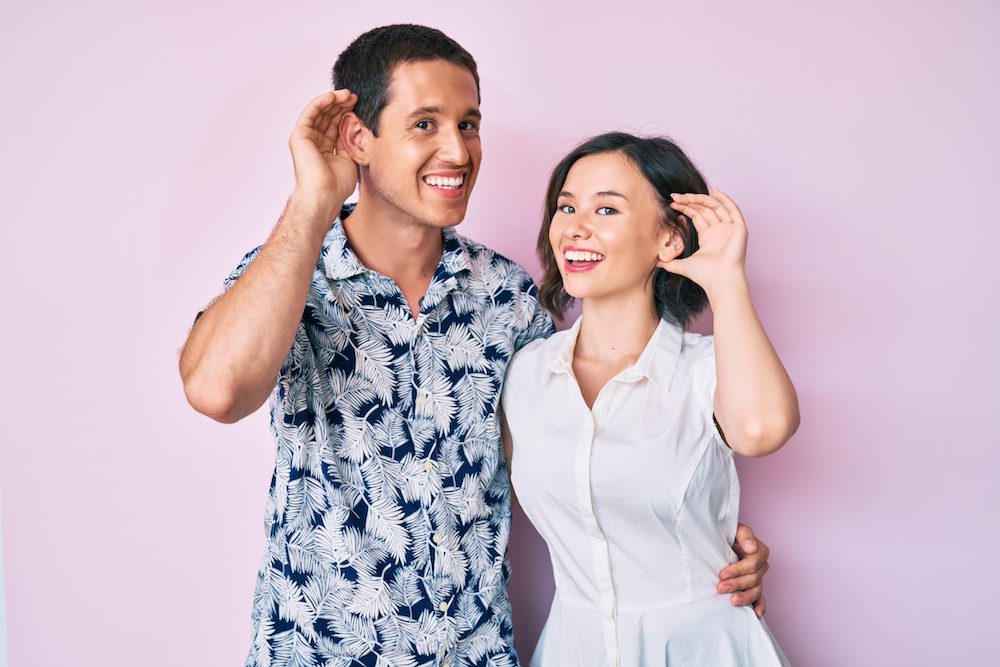 Beautiful couple wearing casual clothes smiling with hand over ear listening an hearing to rumor or gossip. deafness concept.