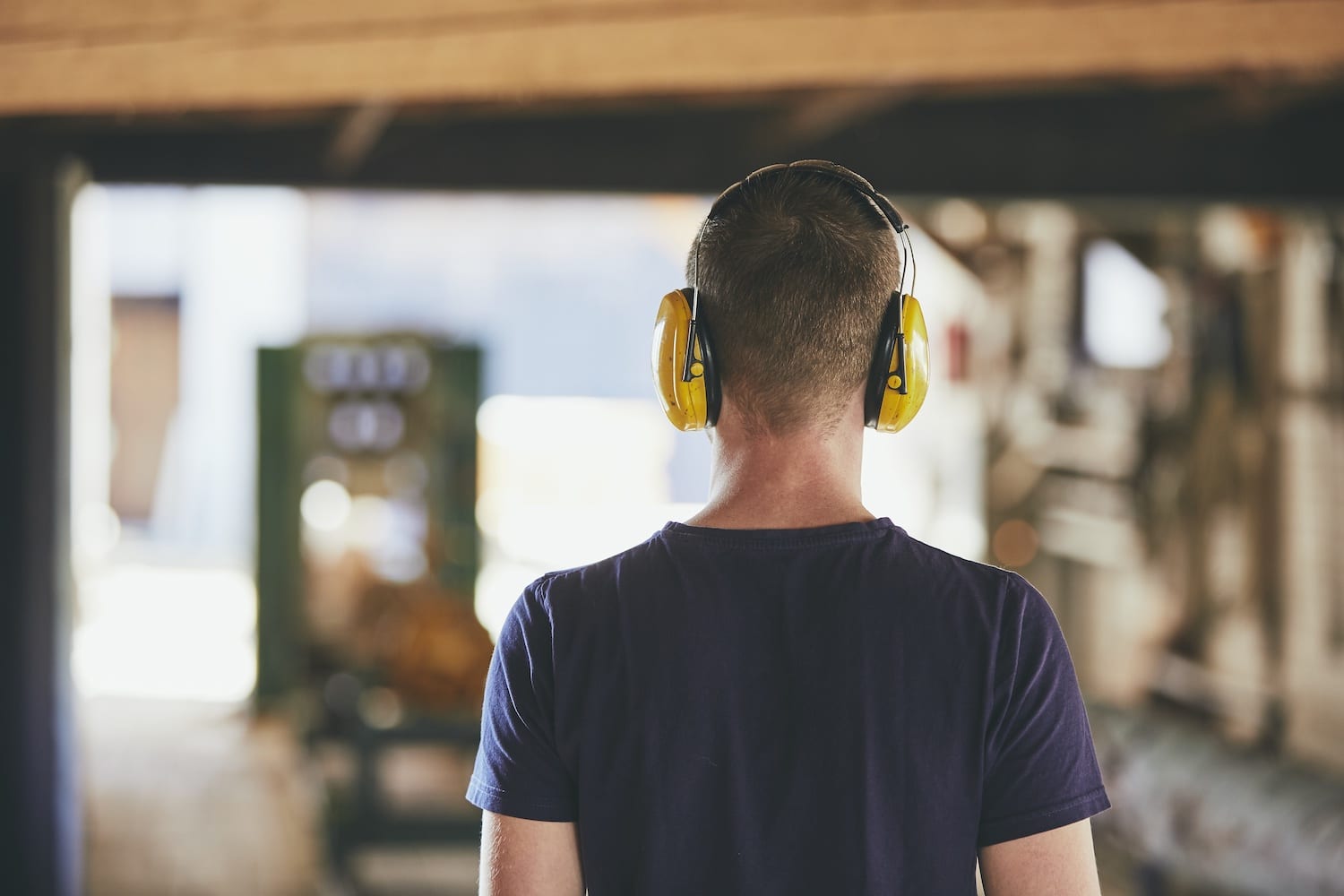Man working in sawmill. Rear view of the worker with headset.