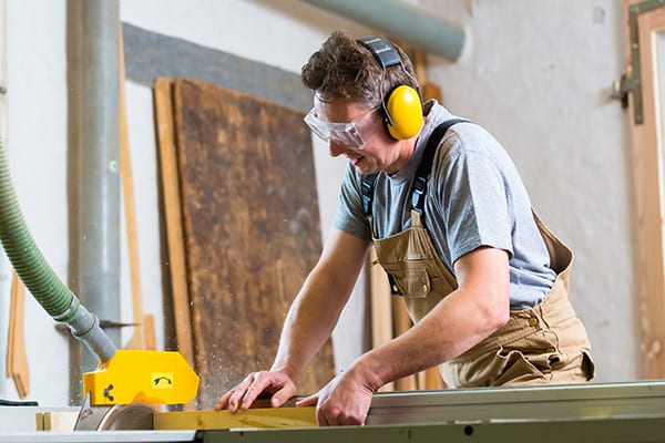 a man wearing ear protection while sawing wood