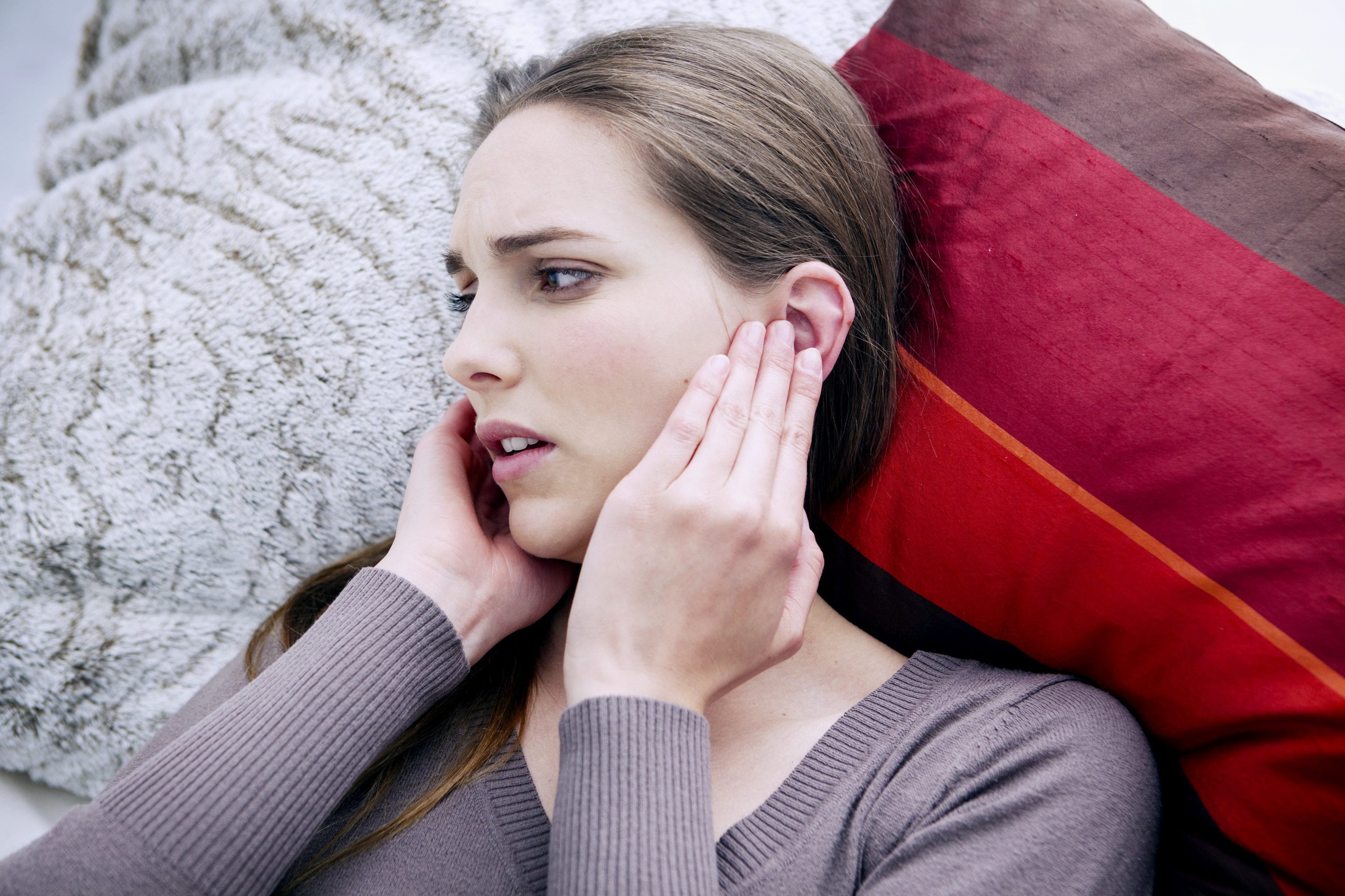 woman lying down in bed wearing sweater with head pains