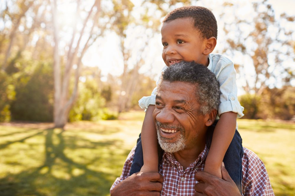 grandpa with grandson on shoulders in backyard on sunny day