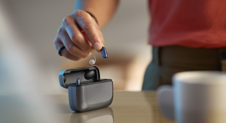 ReSound Vivia holding hearing aid in hand charger on table