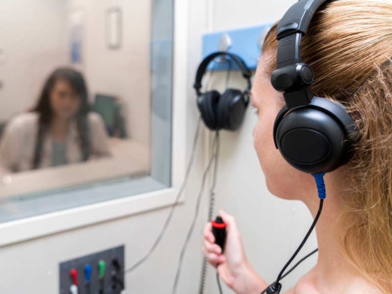 Young woman takes a hearing test in a hearing booth.