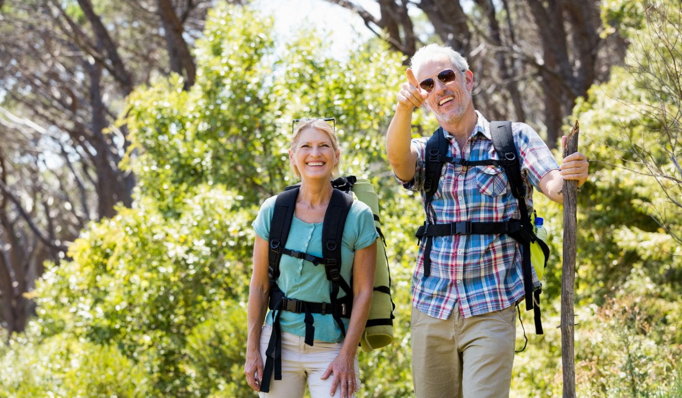 mature couple hiking in blooming forest with gear
