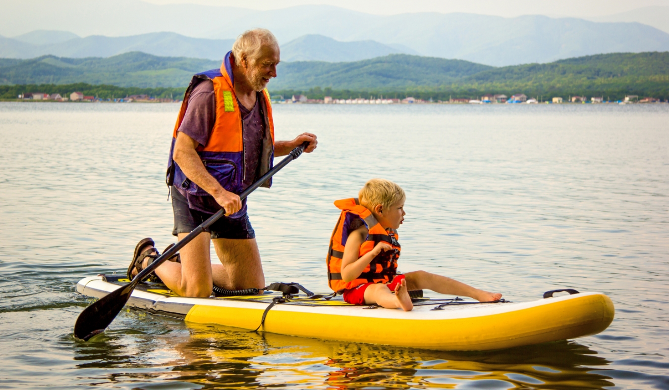 Grandfather and a boy kid in a life jacket ride a paddle board