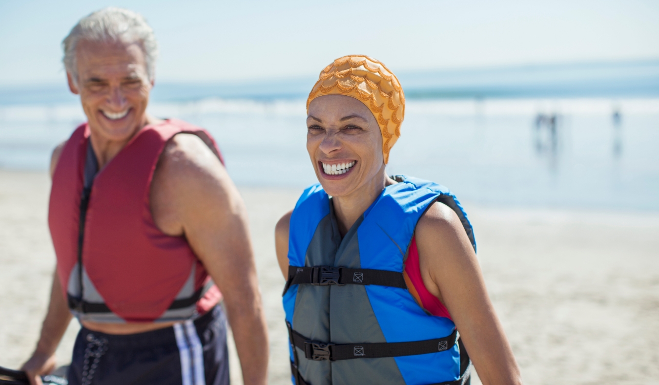 Enthusiastic couple in life jackets on beach