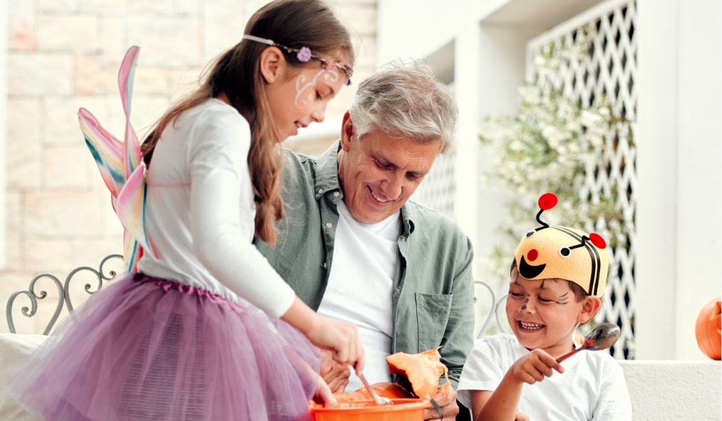 events halloween grandfather carving pumpkin with grandkids dressed up
