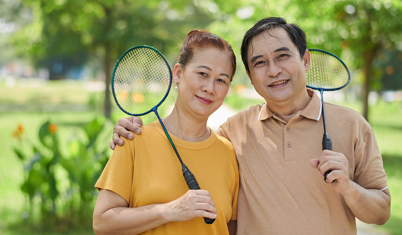 events asian senior couple holding badminton rackets smiling