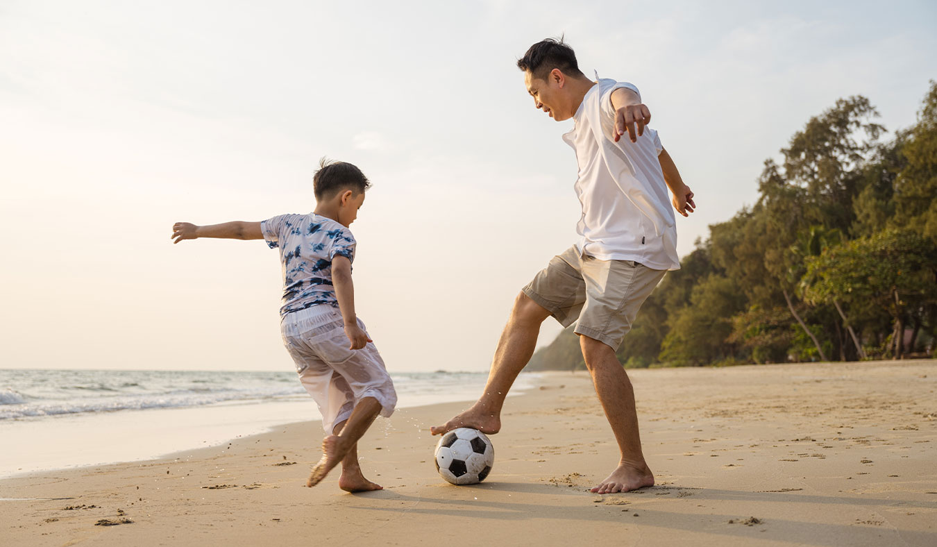 events grandpa playing soccer on beach with grandson
