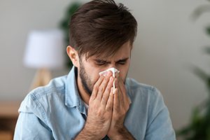 man blowing nose into tissue