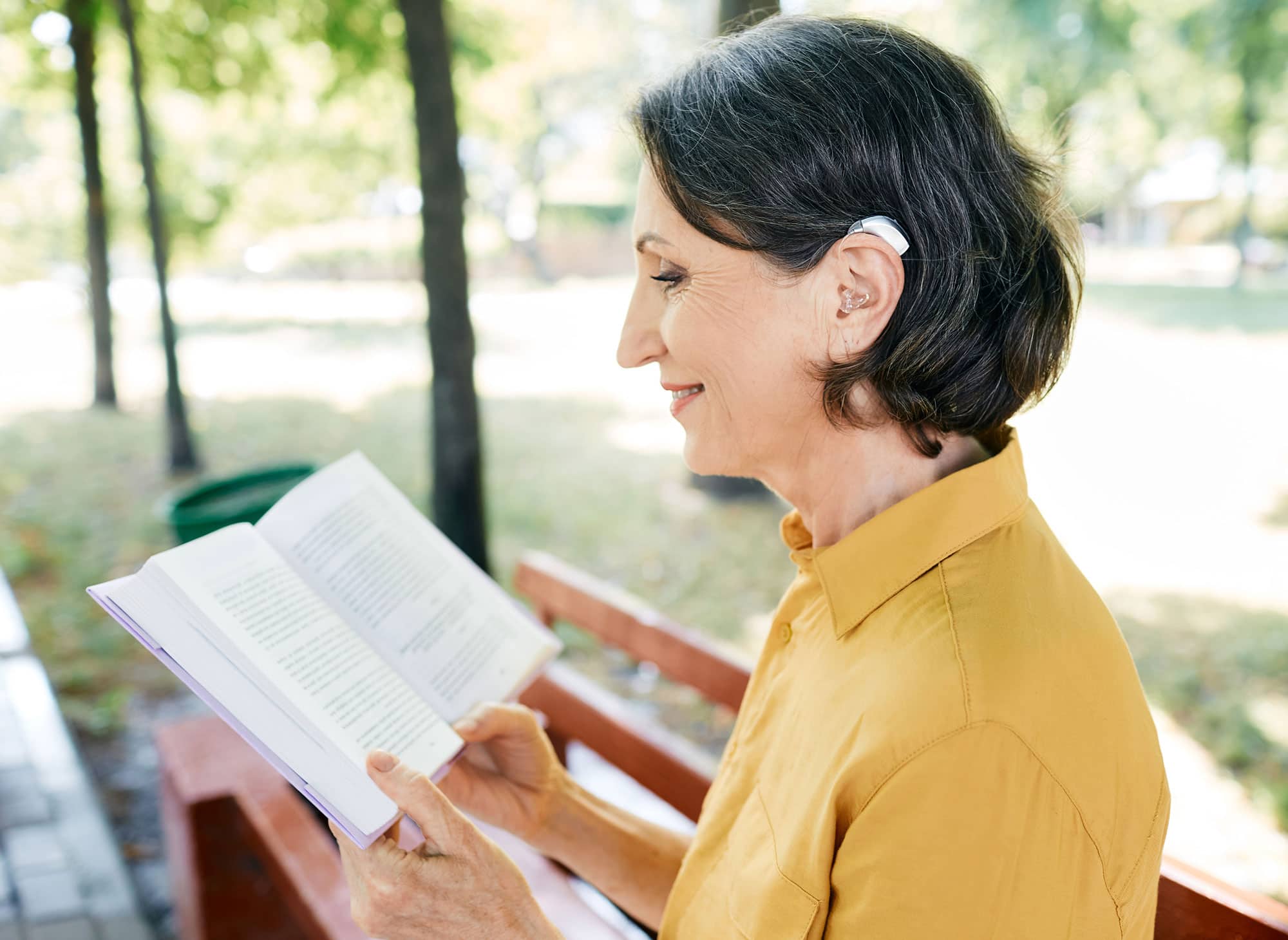 senior woman reading outside wearing hearing aids