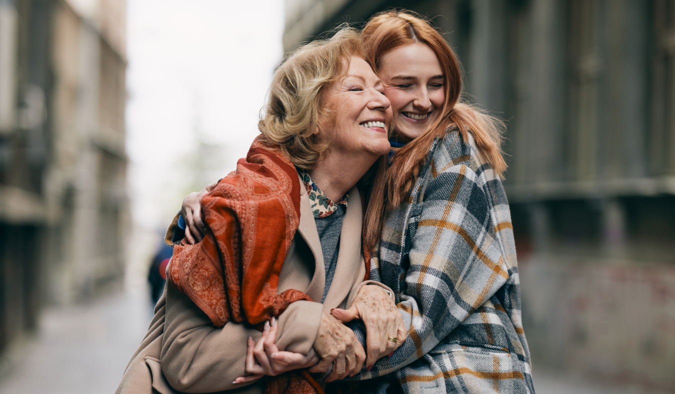 grandmother embracing adult granddaughter dressed for autumn