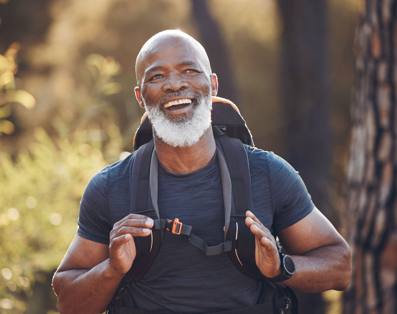 A senior black man hiking in a forest smiling while enjoying nature surrounding him.