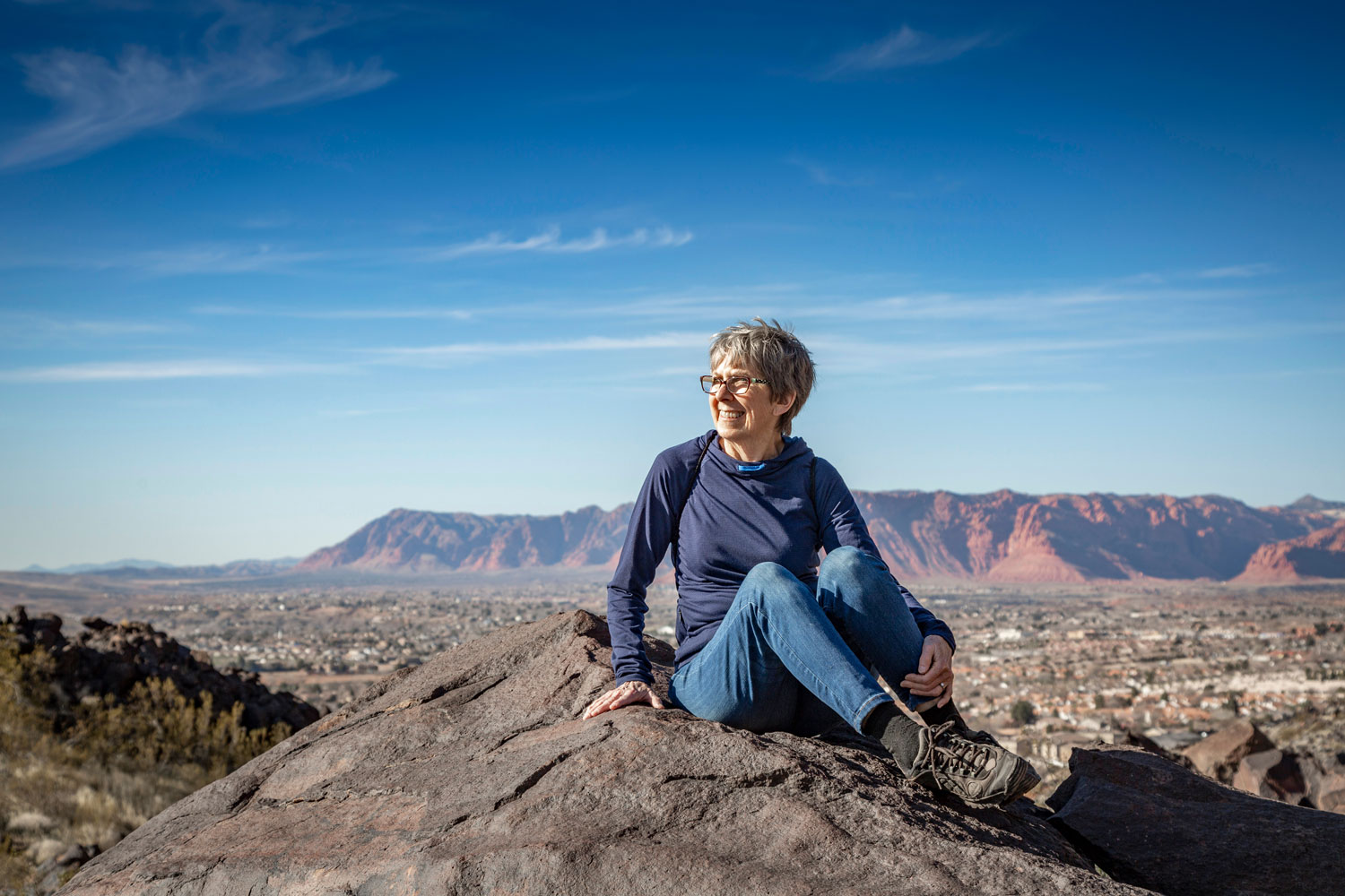 An older woman sitting on rock in an Arizona mountain range admiring the view.