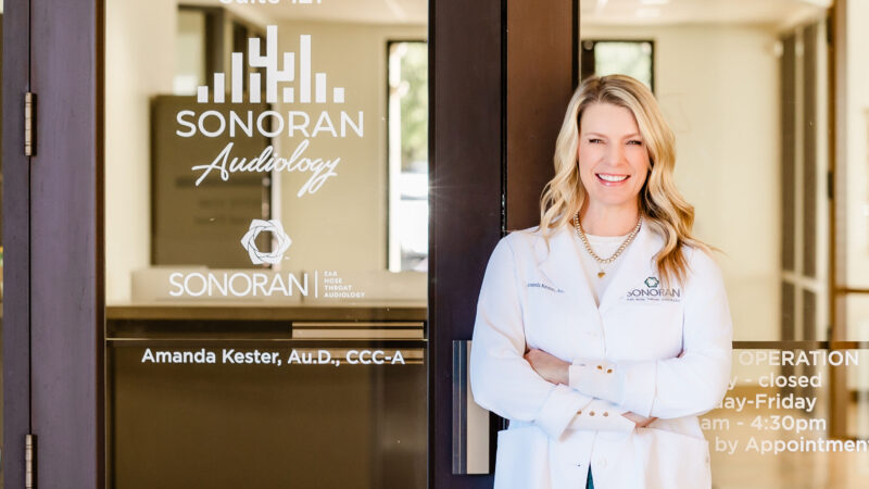 Amanda Kester, AuD standing outside of Sonoran Audiology hearing clinic with the sign and suite number visible on the door.