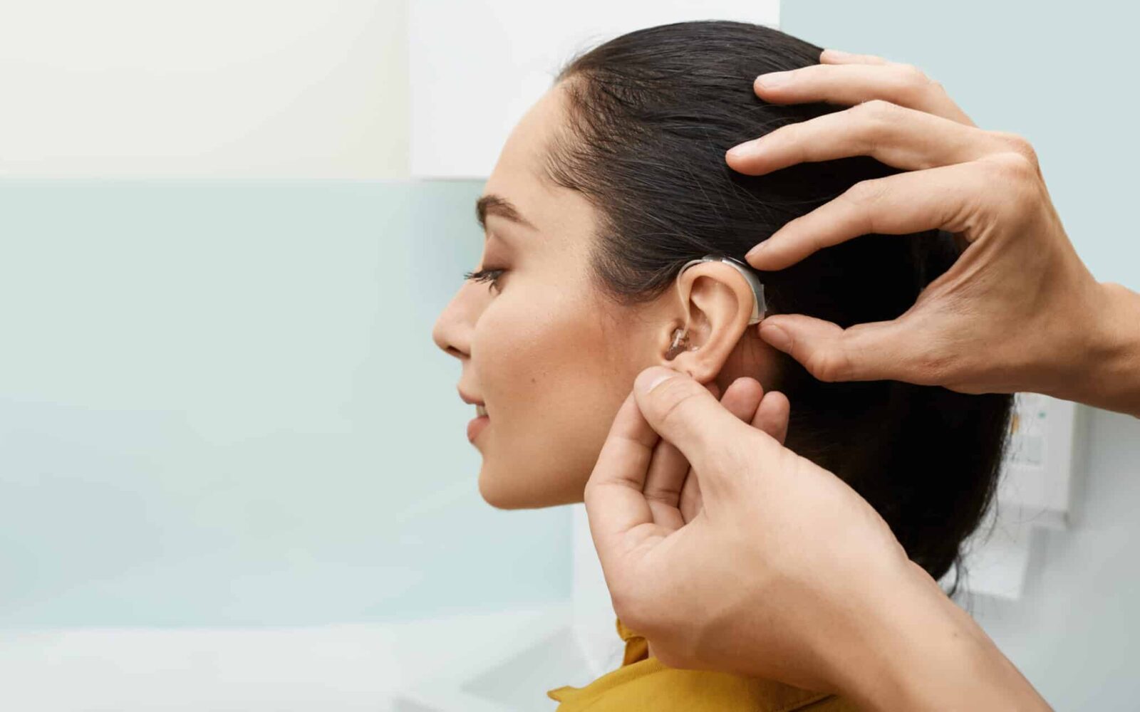Installation hearing aid on woman's ear at hearing clinic, close up, side view Deafness treatment, hearing solutions