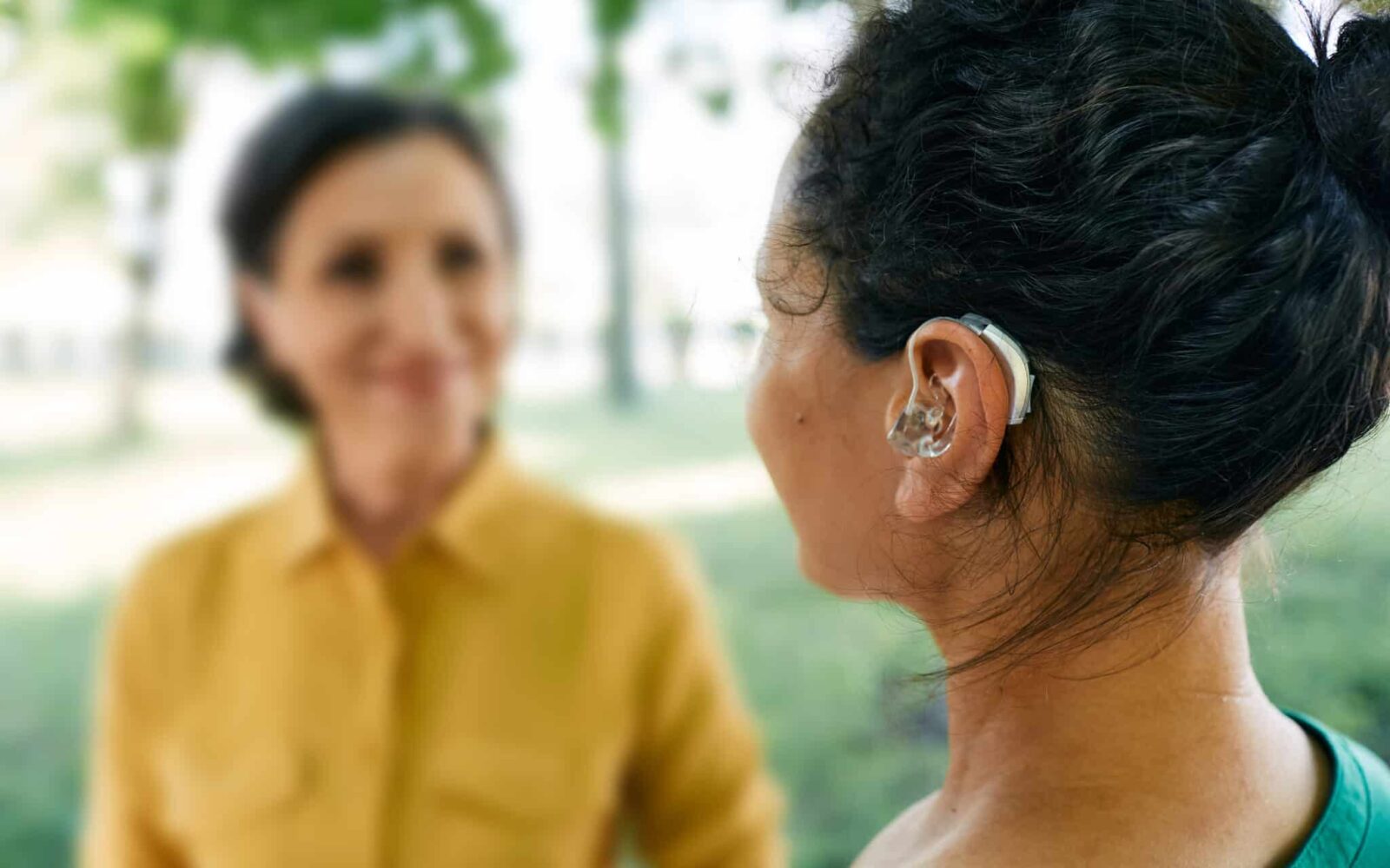 Adult woman with a hearing impairment uses a hearing aid to communicate with her female friend at city park Hearing solutions