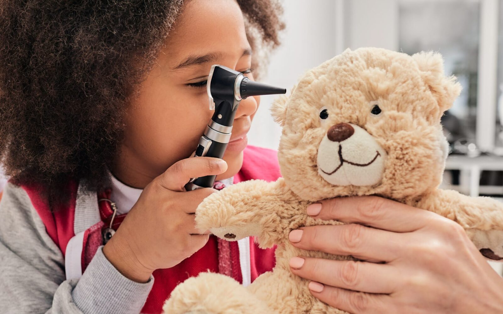 Girl plays with her toy bear in a medical game, using an otoscope Hearing clinic for children