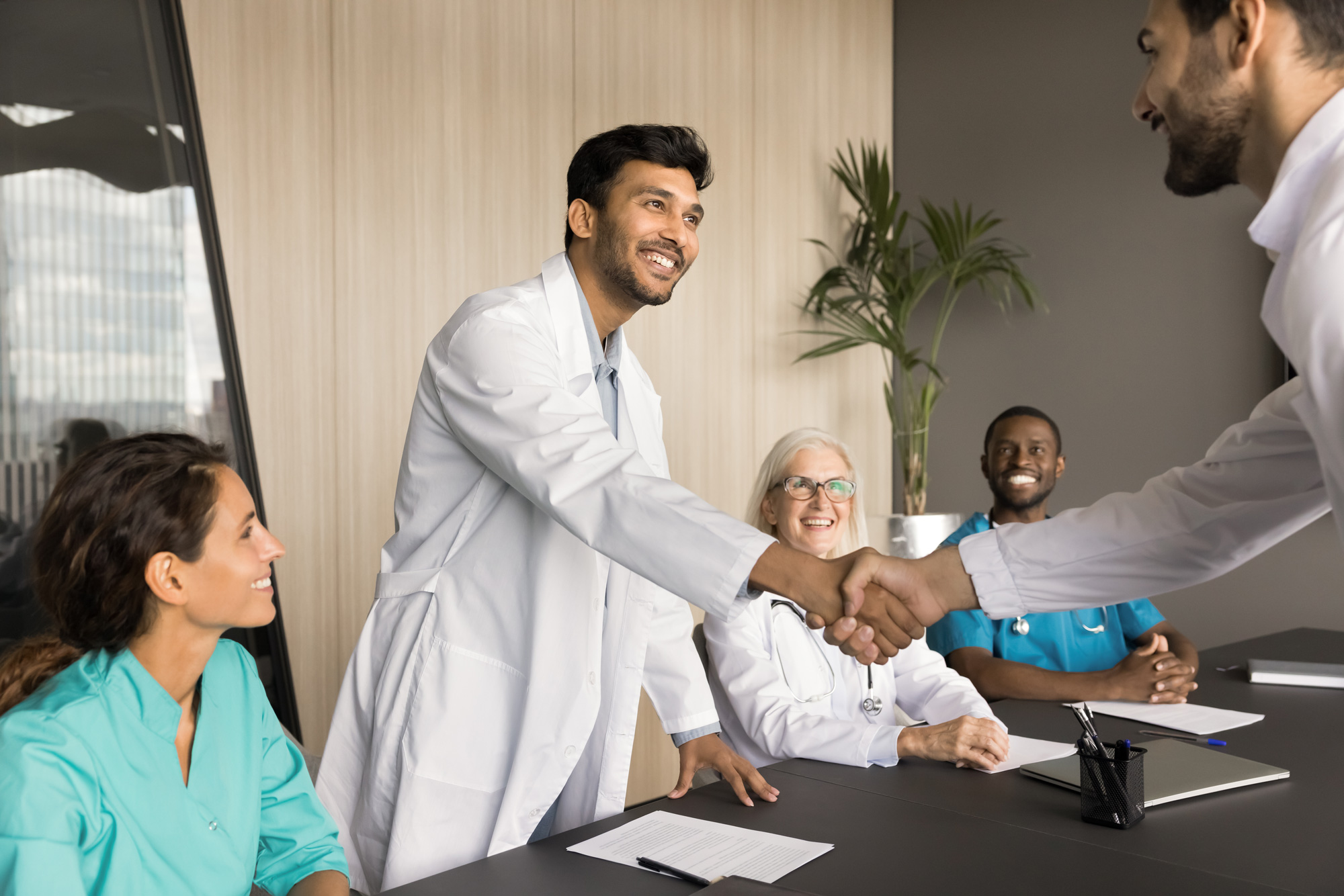 male doctor shaking hands with medical professional man surrounded by diverse doctors