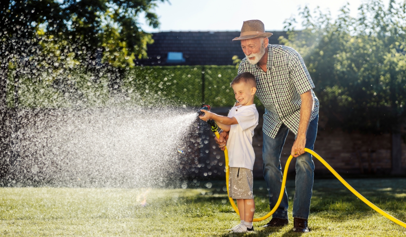 grandson and granddad watering lawn in backyard together