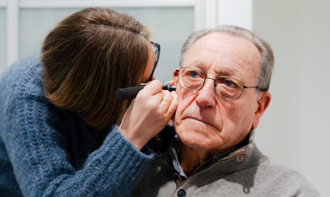 audiologist inspecting senior patient ear with otoscope