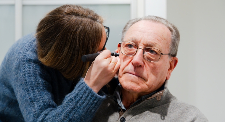 audiologist inspecting senior patient ear with otoscope