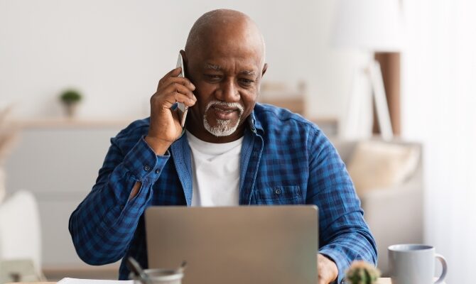 senior male using laptop and phone to schedule
