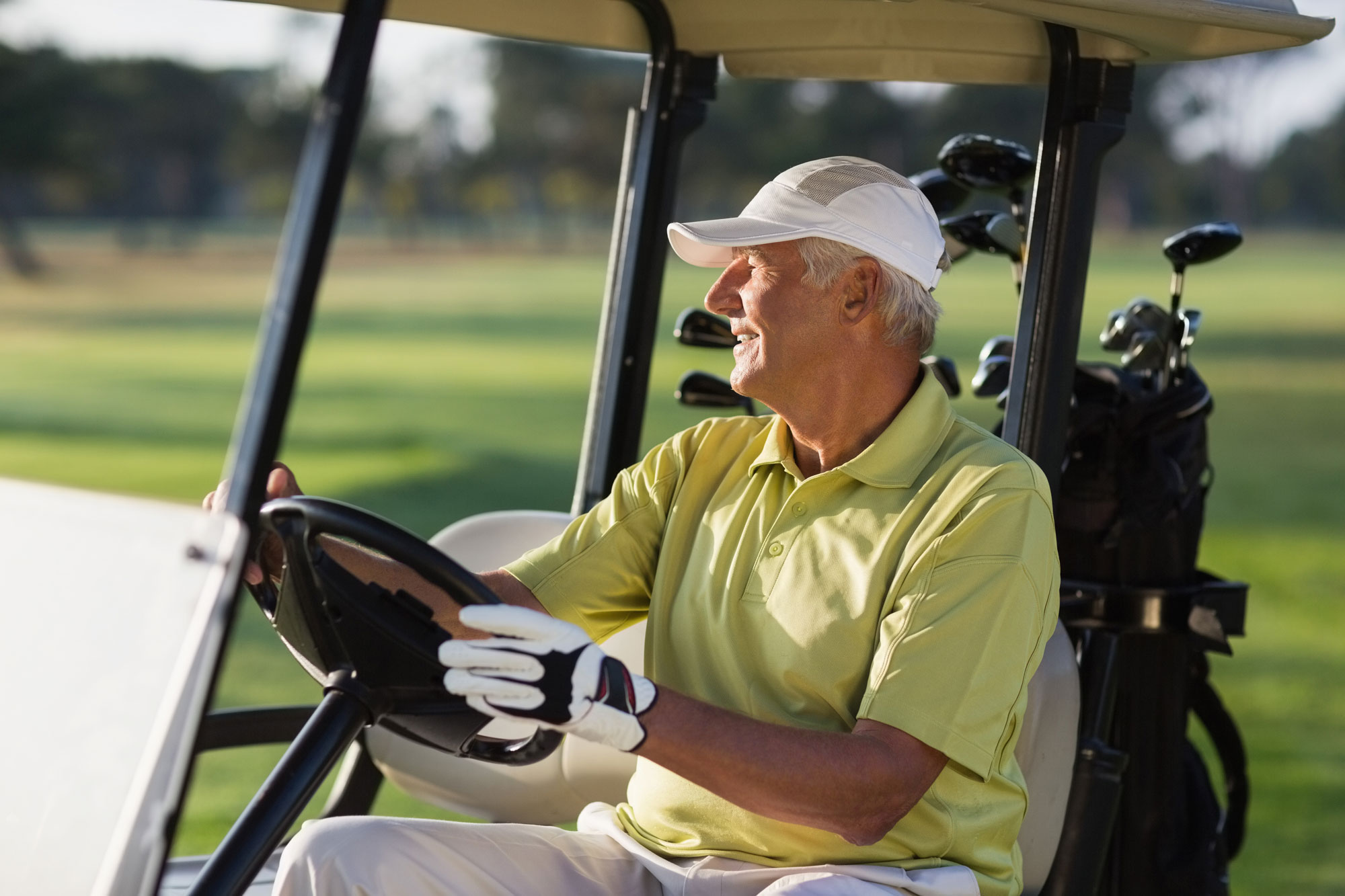 Smiling mature man driving golf buggy on field