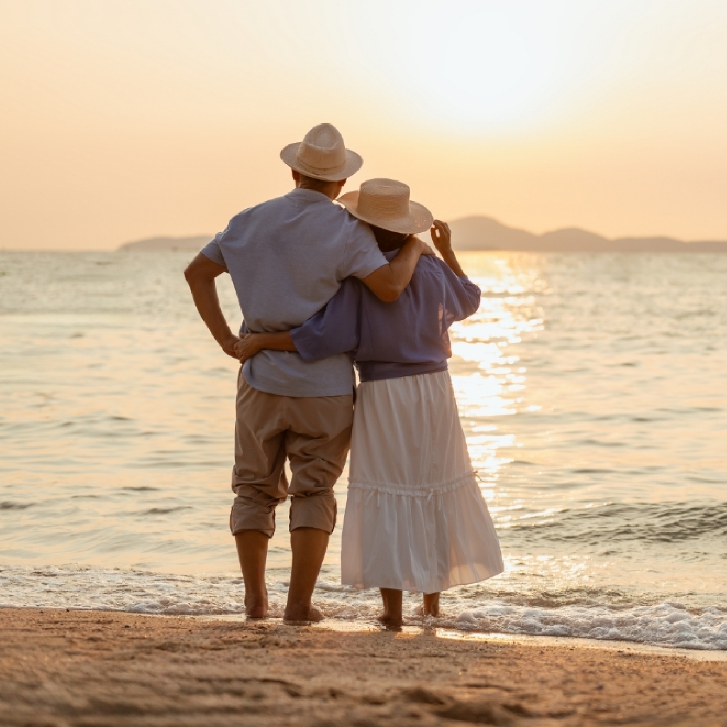 a couple standing on the beach at sunset