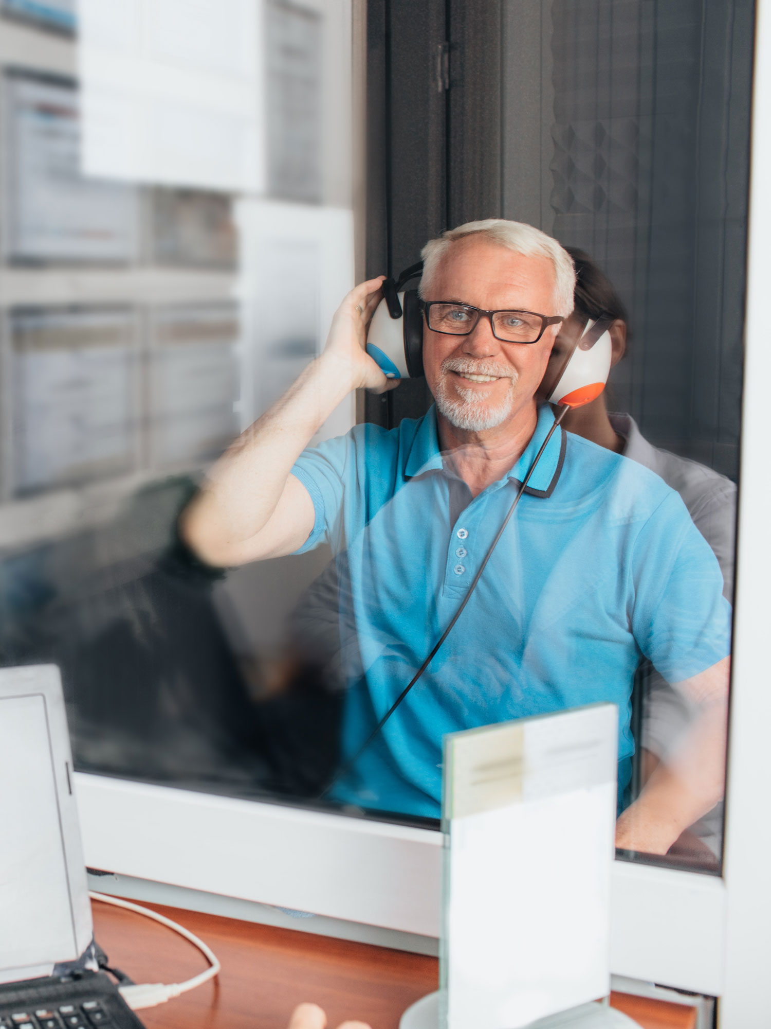 senior man taking hearing test inside booth