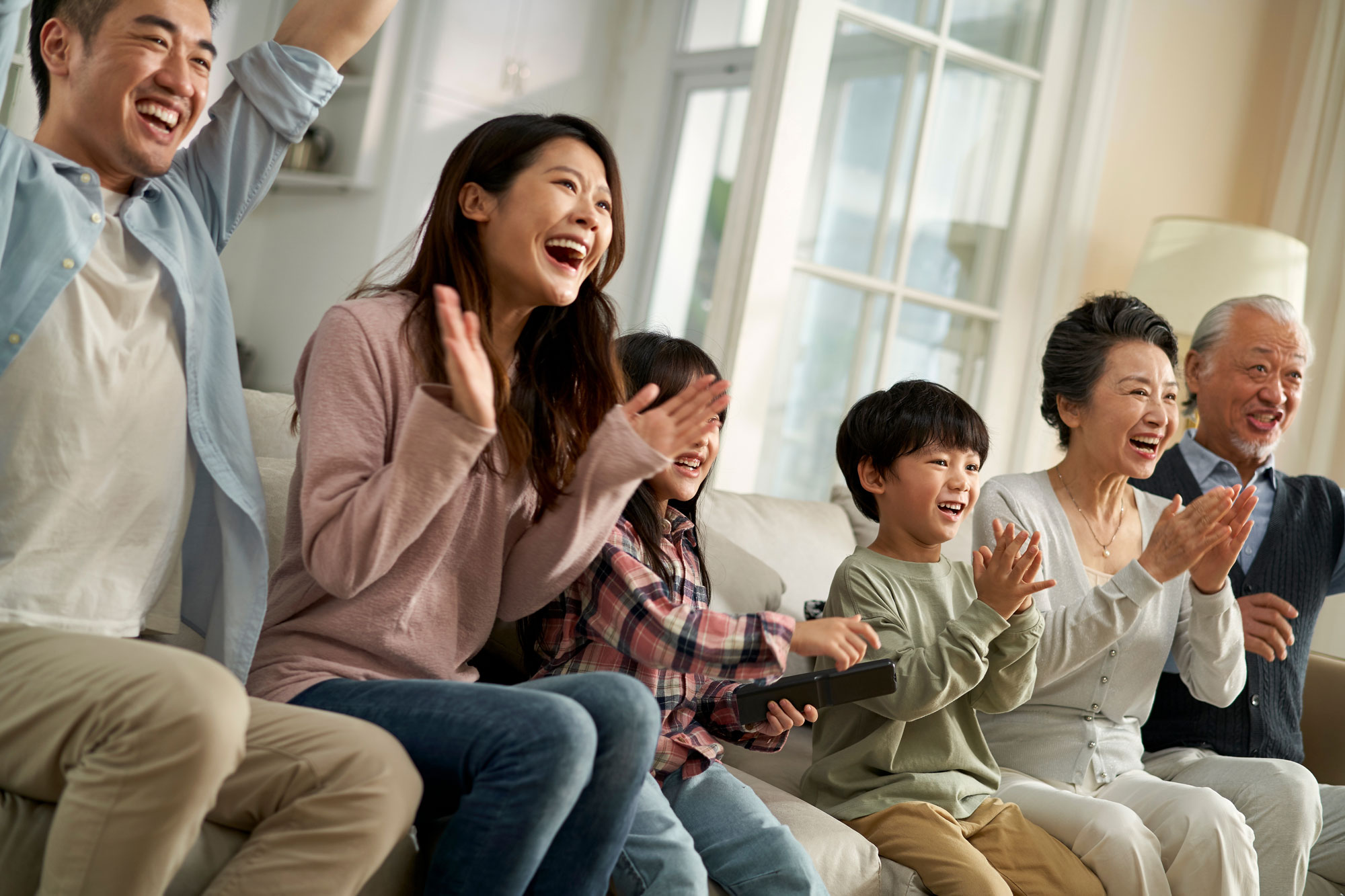 three generation family sitting on couch watching tv excited