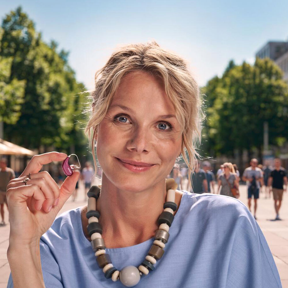 oticon reveal woman holding hearing aid smiling