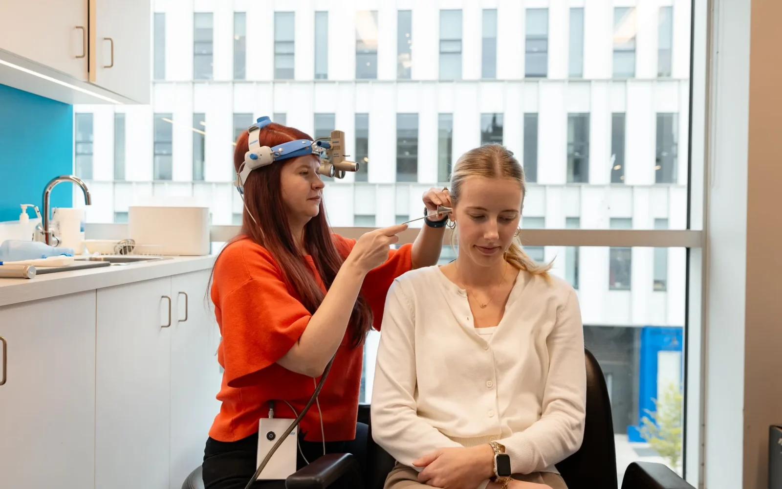Healthcare professional using an otoscope to examine a patient's ear in a clinical setting.