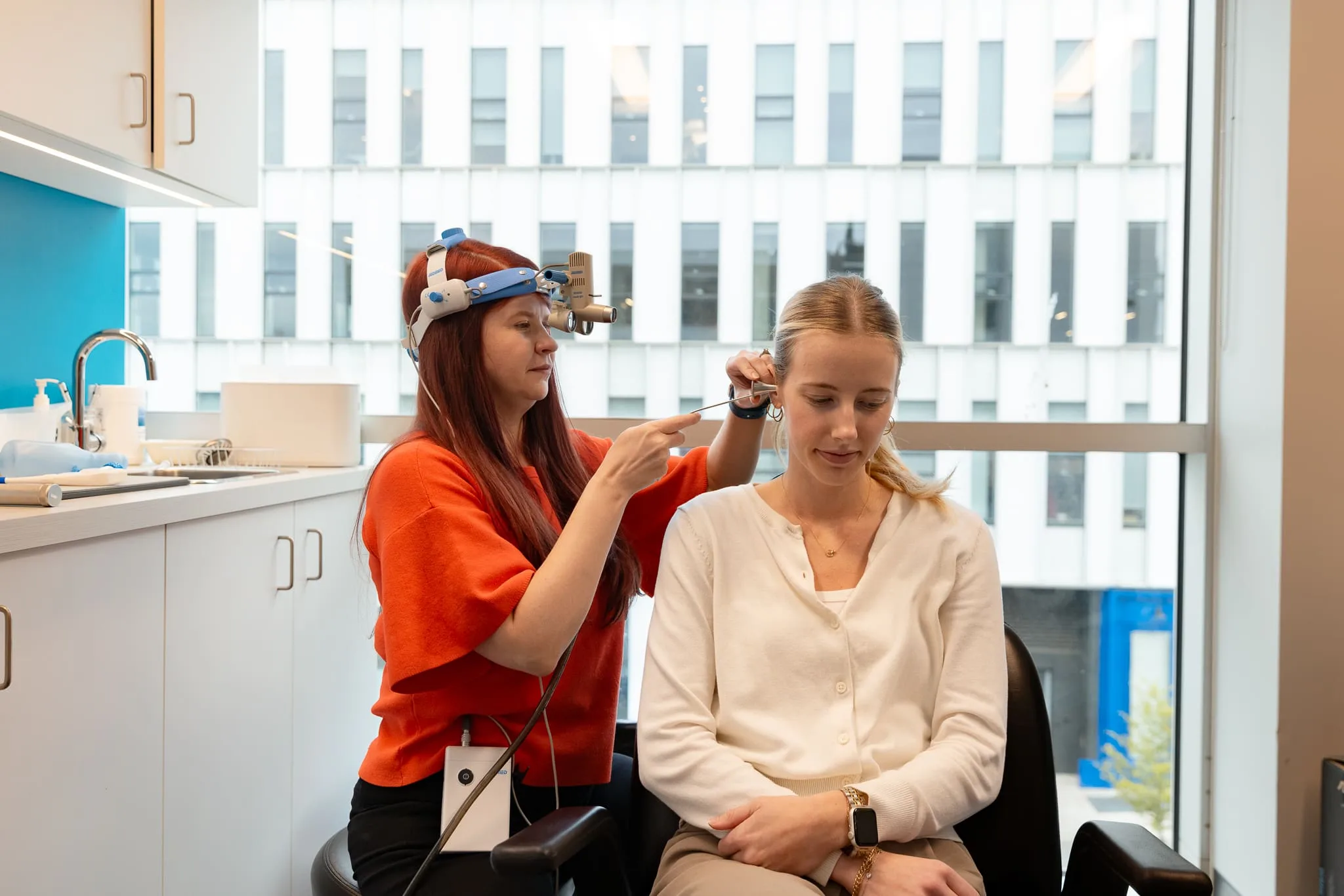 Healthcare professional using an otoscope to examine a patient's ear in a clinical setting.