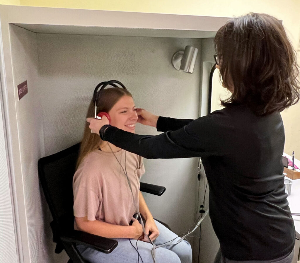 dr andi placing headphones on womans head in sound booth
