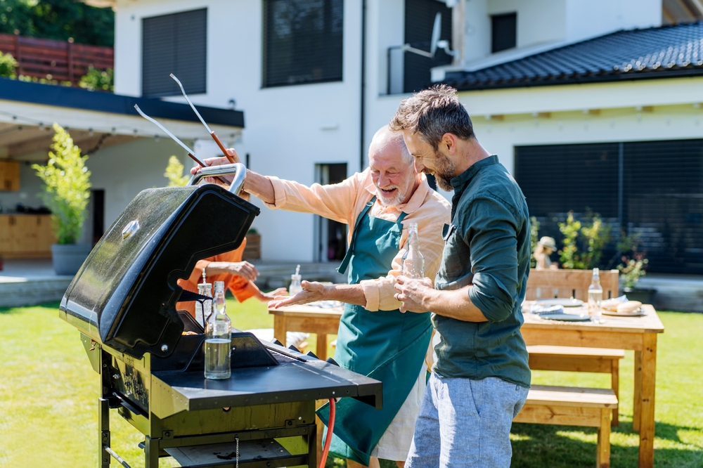 Senior,Father,With,Adult,Son,Grilling,Outside,On,Backyard,In