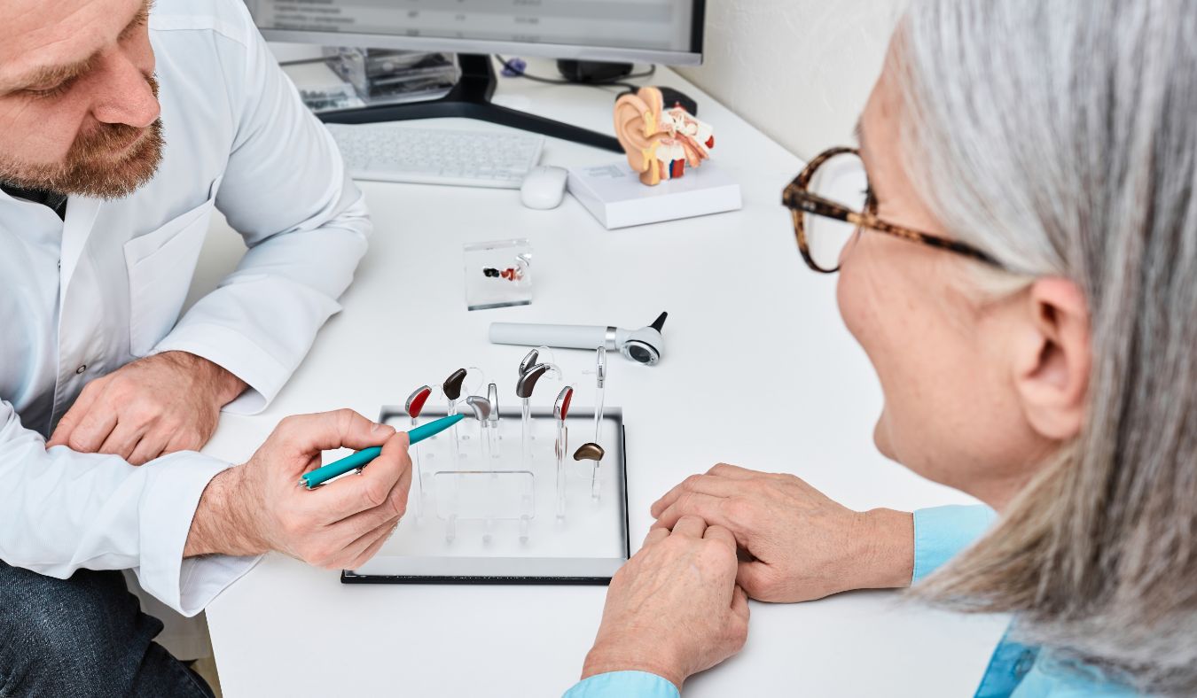 Hearing specialist showing different hearing aid models to an older person during consultation.