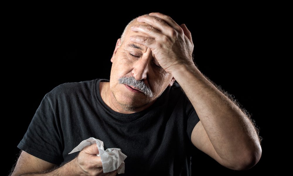 man blowing nose into tissue