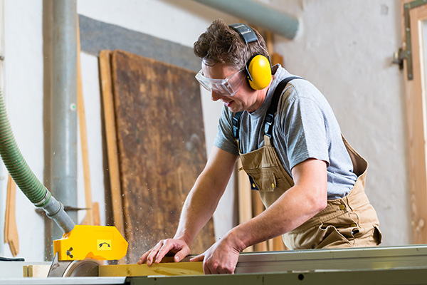 a man cutting wood in his garage while wearing proper hearing protection