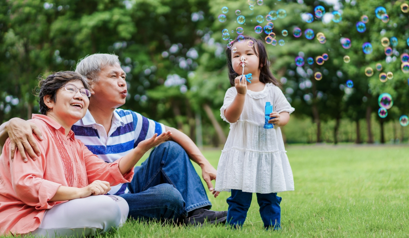 asian granddaughter blowing bubbles with grandparents in park