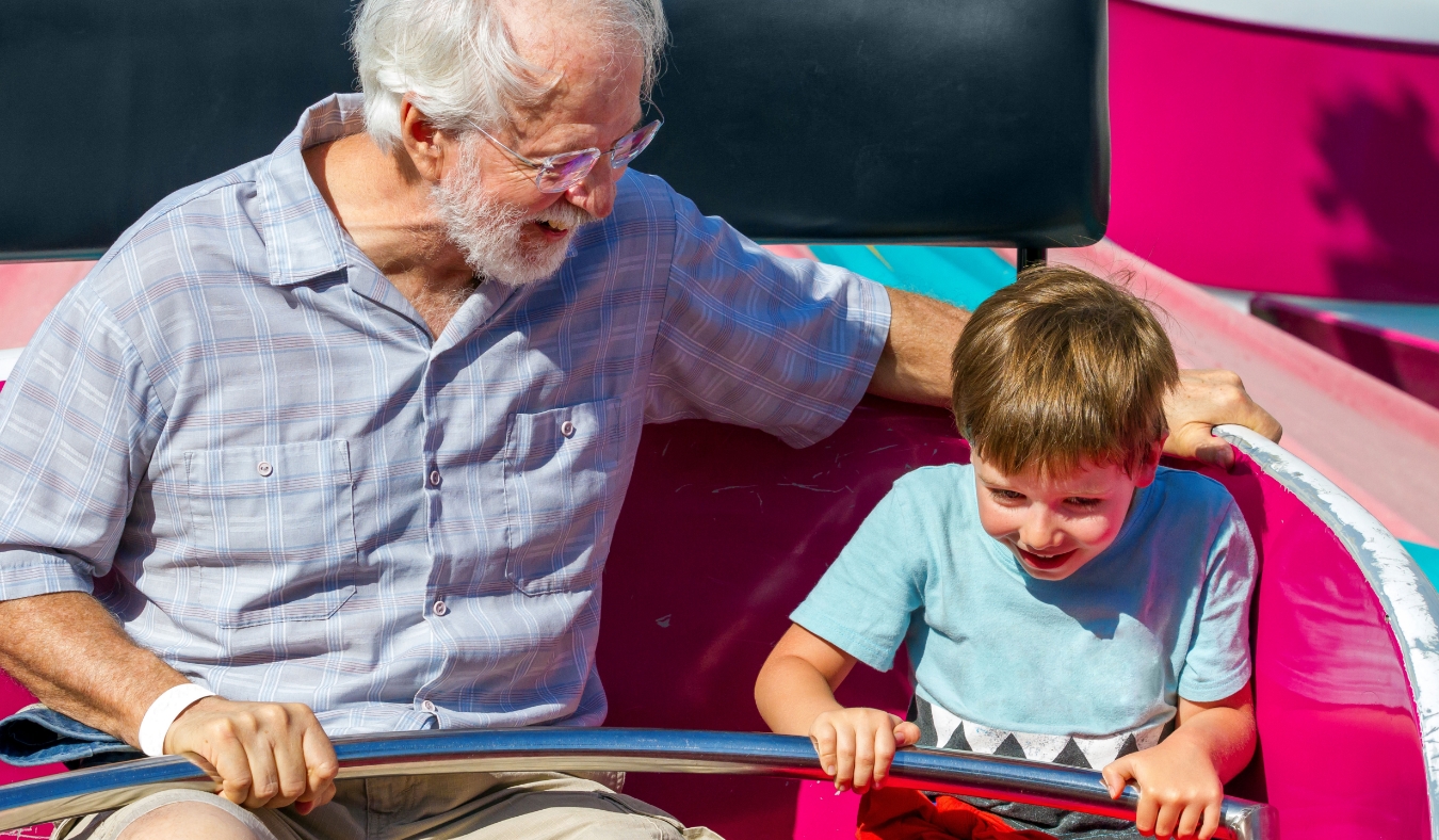 elderly man and his young grandson ride a carnival ride at a theme park