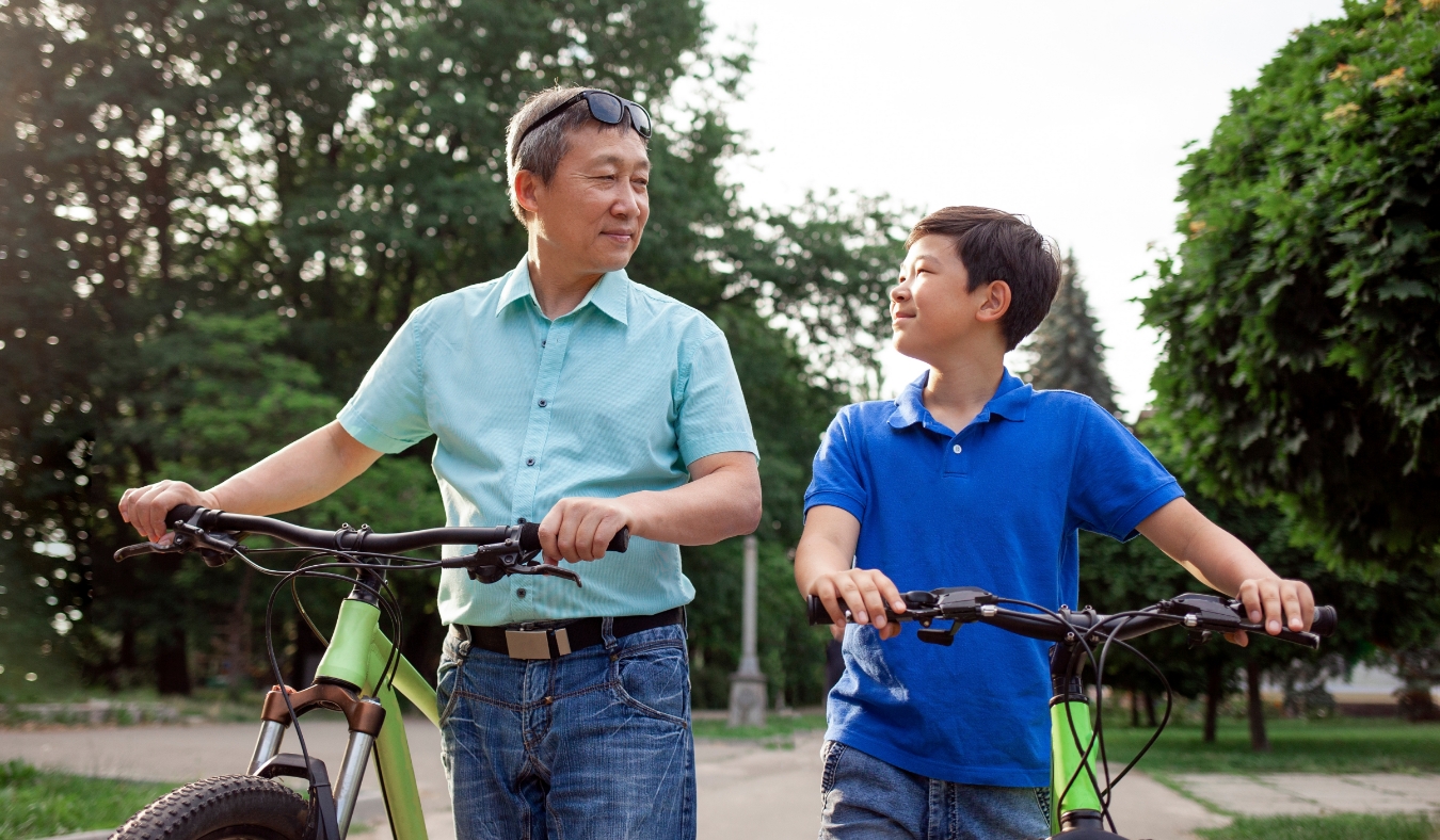 asian old father and son ride bikes together in the park