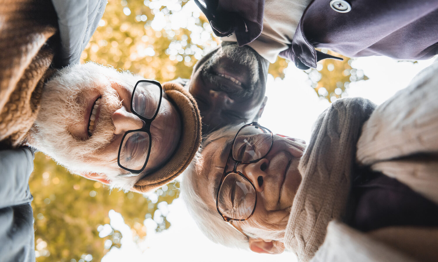 Bottom view of multicultural friends in eyeglasses looking at camera outdoors