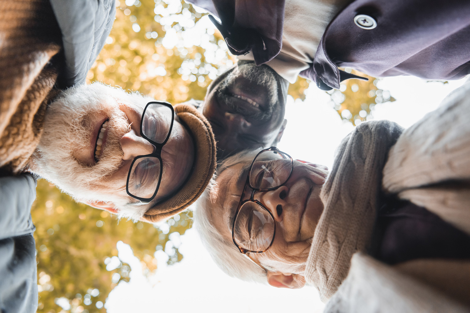 Bottom view of multicultural friends in eyeglasses looking at camera outdoors